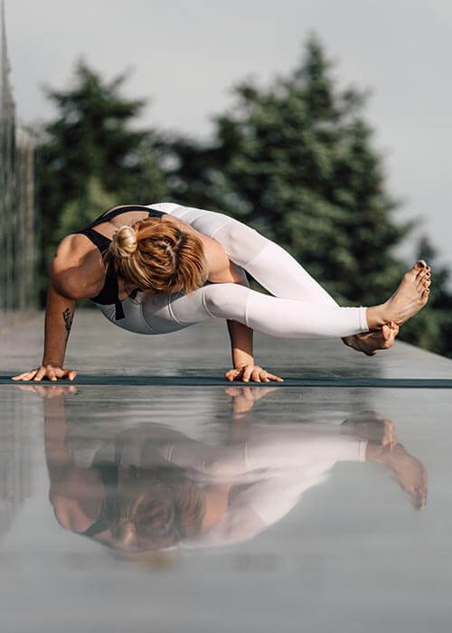 Vêtement de yoga dynamique Ashtanga et vinyasa - Yogini réalise la posture de la pince sur une terrasse | Achamana